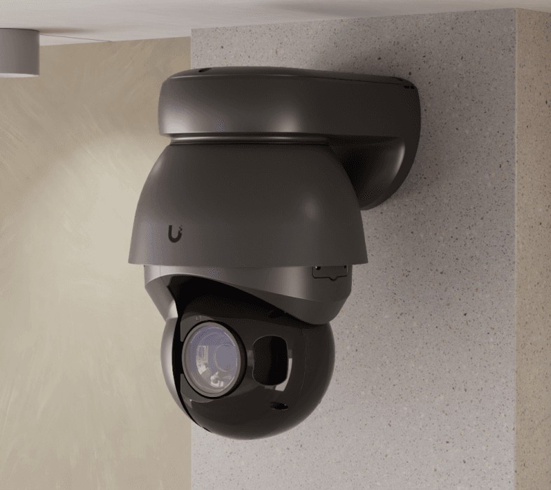 Black UniFi AI PTZ Precision 4K PTZ camera on a wall-arm mount at the corner of a building pillar